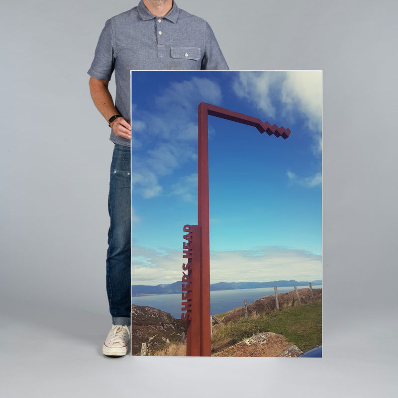 A man from The Canvas Works stands besde a large portrait shape canvas print measuring 80x120cm. The print features a scene from The Wild Atantic Way in West Cork. 