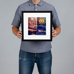 A man holds a black-framed photo print with a white mat. The print features a 2x2 collage photo grid of famous Dublin pubs. The print is 20x20cm and the frame is 34x34cm.  