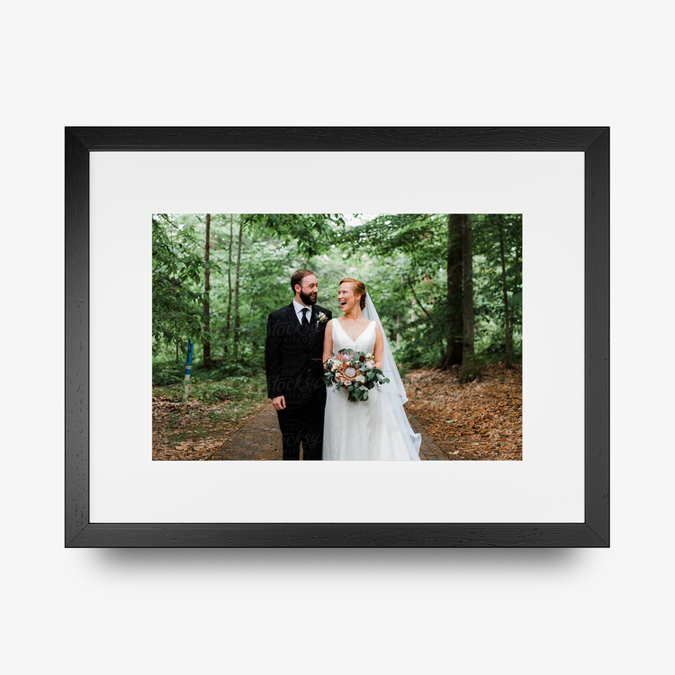 A rectangle shaped framed print in a black frame featuring a smiling bride and groom.