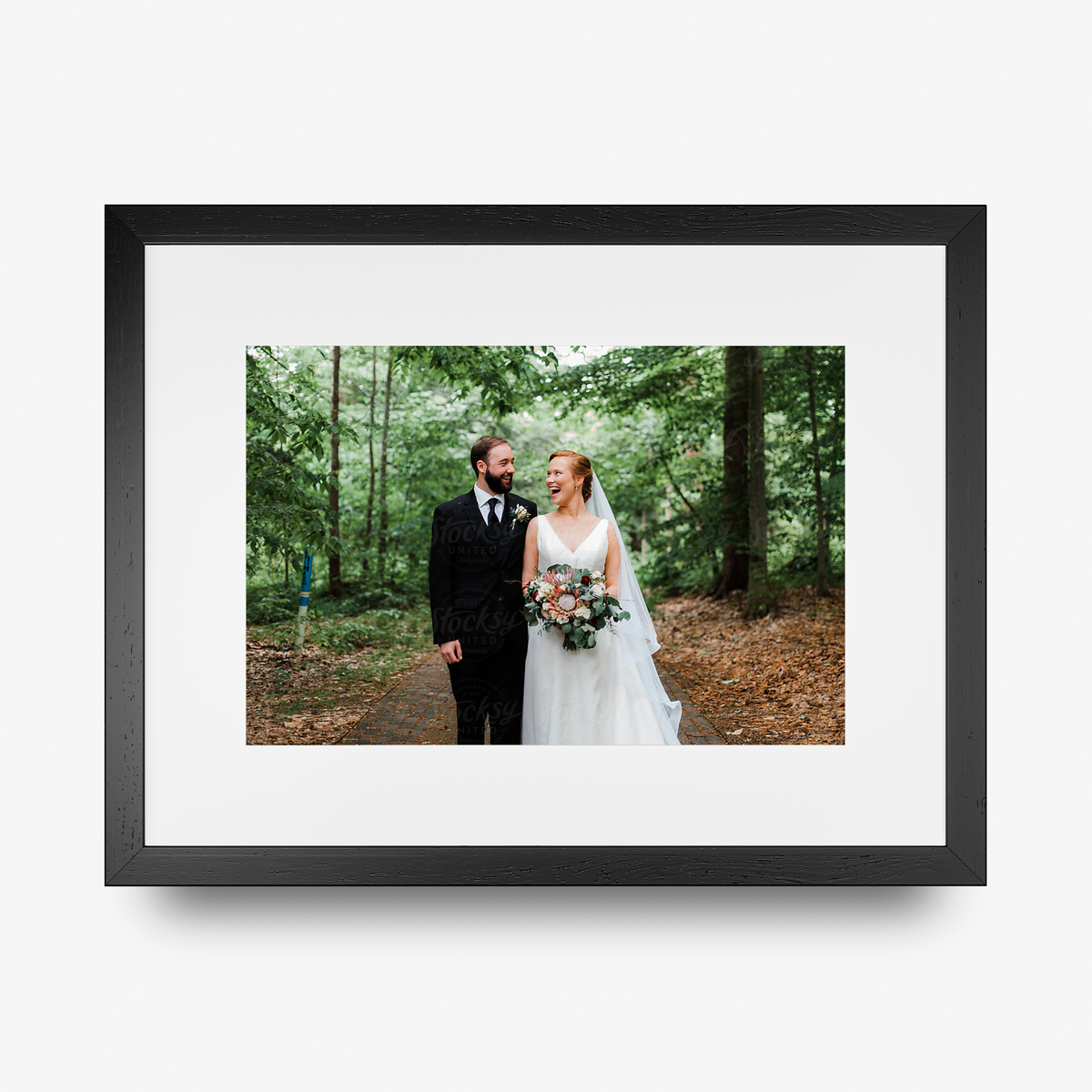 A rectangle shaped framed print in a black frame featuring a smiling bride and groom.