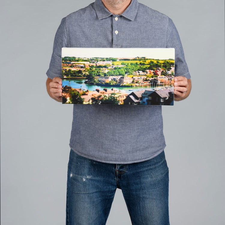 A man holding a panoramic shaped canvas print featuting Kinsale harbour. 